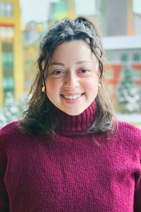 A headshot of a woman in a red sweater with the Minneapolis skyline in the background