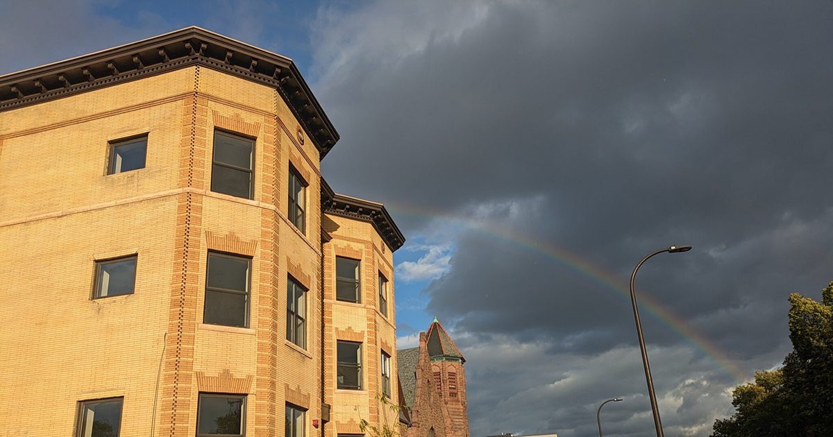 A pale brick apartment building with a rainbow in the background