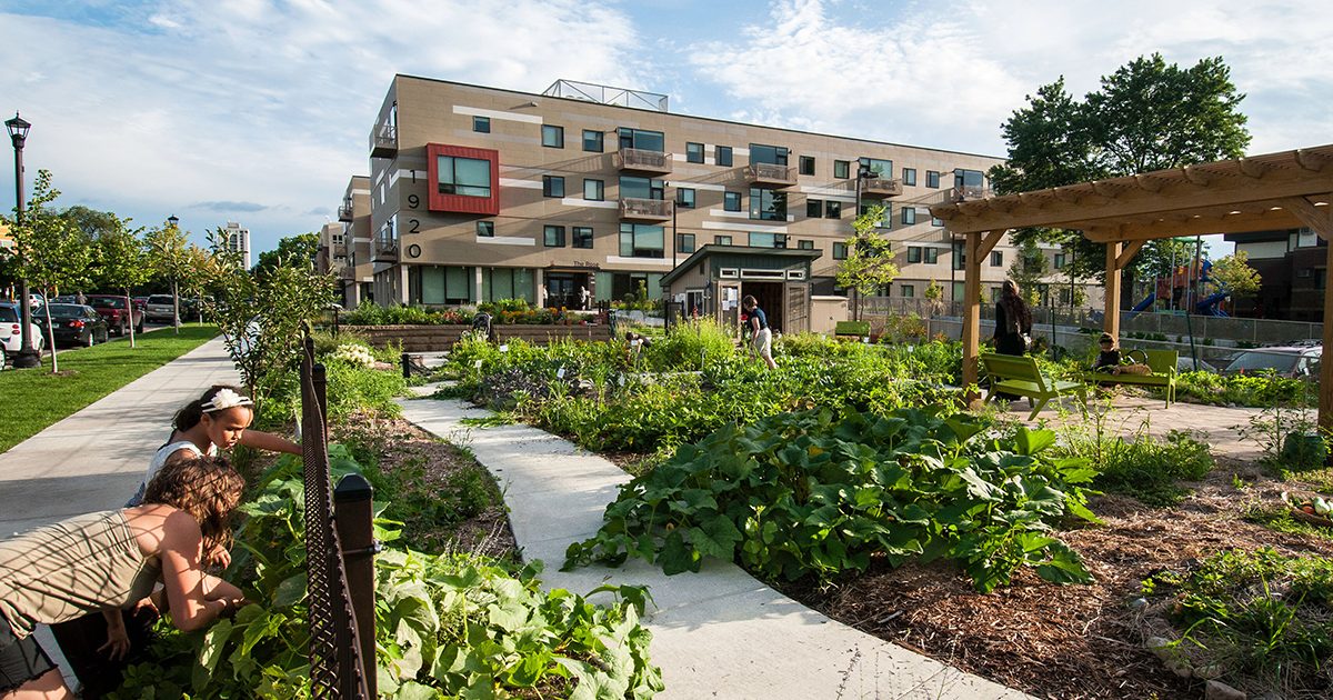 A woman and child gardening outside a large apartment complex with a large garden