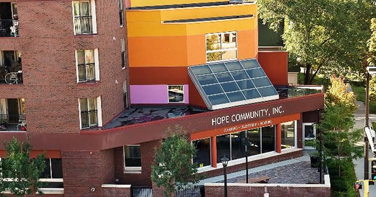 Aerial photo of a large brick building with orange and purple painted accents and solar panels. The front awning says "Hope Community, Inc."